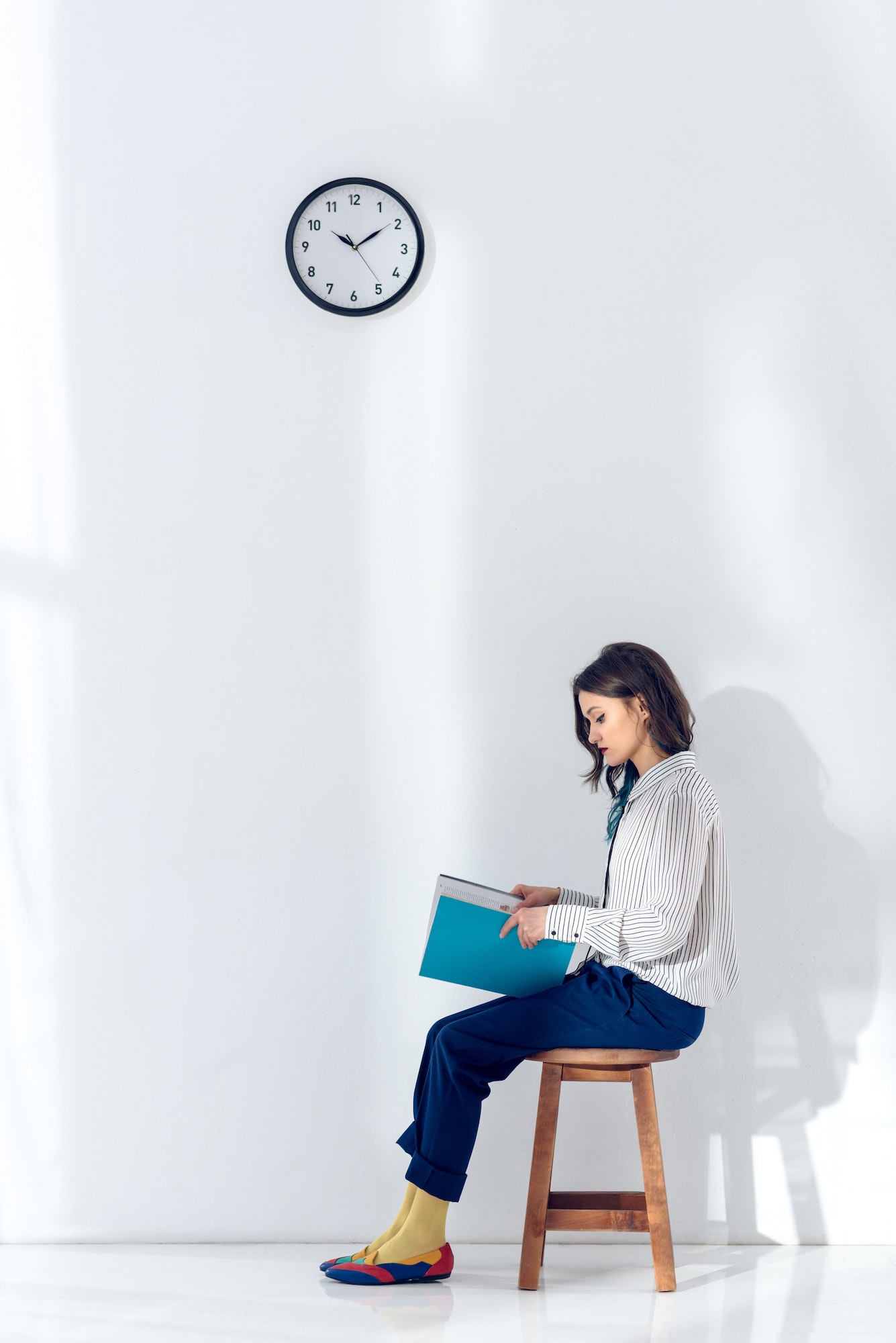 Attractive young girl sitting on chair and reading book under clock