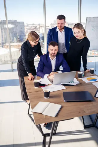 Happy business people looking at laptop presentation, success at work, sitting in modern office. Successful online negotiations. Businessmen share their knowledge