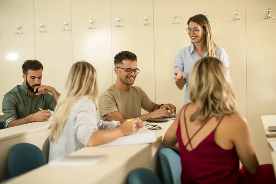 Group of university students in the classroom with young female assistant lecturer